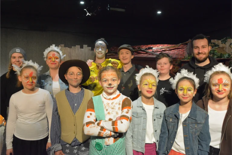 Gruppe von Schauspielern der Ruhrbühne Witten mit bunten Gesichtsmalereien und Kostümen vor der Bühne