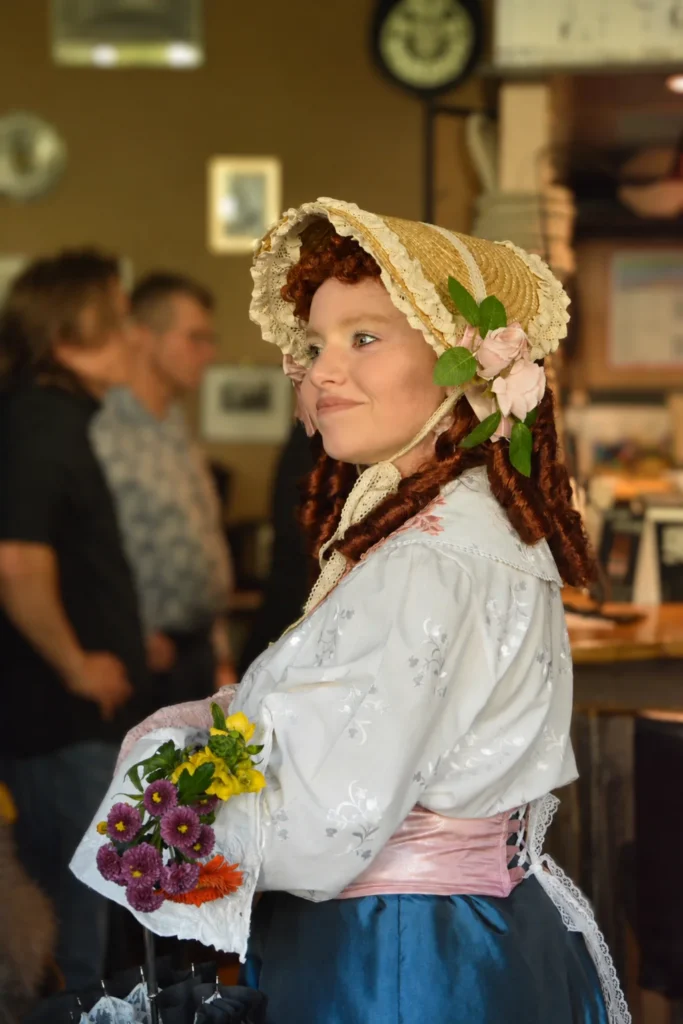 Porträt einer Darstellerin aus Pension Schöller mit blumengeschmückter Haube und buntem Blumenstrauß